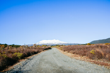 Gravel road and Mount Ruapehu snow capped under blue sky in wide landscape