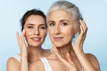 Two women of different ages and skin types take care of their facial skin, apply moisturizer, and...