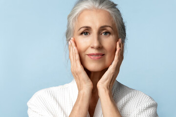 A beautiful elderly woman with perfect skin and gray hair touches her face with her hands. A mature...