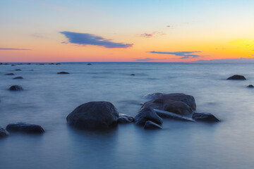 Fototapeta na wymiar A beautiful scene of sunset sky reflecting on water with boulders of Baltic sea shore