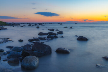 Fototapeta na wymiar Blue hour after the sunset over rocky Baltic sea cost. Small stones and big boulders in the sea. Long exposure photo.