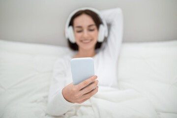 Mobile phone in young woman hand, bedroom interior