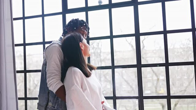 Interacial couple hugging, looking through the window wall. High quality 4k footage