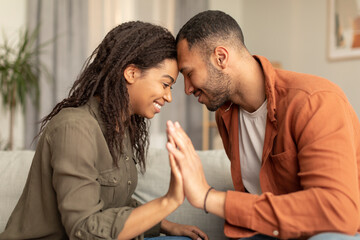 Romantic african american spouses holding their hands, touching foreheads, bonding while sitting on sofa