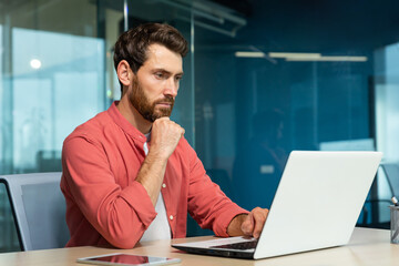 Serious thinking businessman close up, man in red casual shirt working inside modern office, mature...