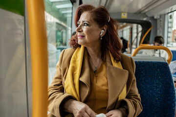 mature woman listens to music with headphones while traveling in public transport on the way to work