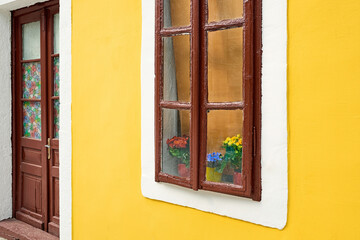 Obraz premium View of the old door and window. Beautiful flowers on the windowsill in the window.
