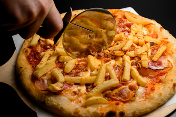 hand accurate cuts with a pizza cutter hot pizza with french fries and bacon slices.
