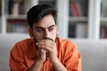 Pensive young arab man sitting on sofa at home