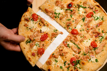 Top view on pizza with topping of cherry tomatoes and chicken and hand taking a piece of it