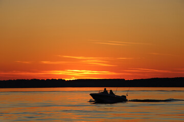 Silhouette of two fisherman on the boat. Beautiful sunset on the background.