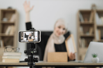 Focus on smart phone screen, pleasant arab woman filming video on modern phone camera while opening parcel box. Concept of people, technology and blogging.