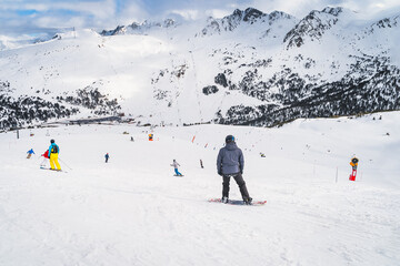 Fototapeta na wymiar Snowboarders and skiers riding down the mountain towards valley below with snow capped mountain peaks in background, Andorra, Pyrenees