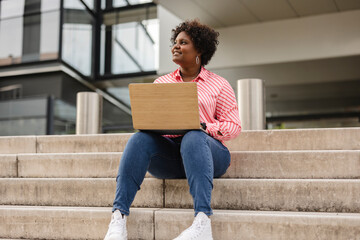 Focused young African college student working on a laptop on some stairs on campus preparing for an exam