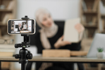Fototapeta na wymiar Focus on phone screen , muslim woman recording video on phone camera while unpacking box with new wireless tablet. Female influencer sharing with subscribers her positive feedback about new order.