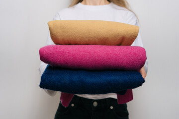A young woman holds three warm woolen sweaters of different colors in front of her on a white...