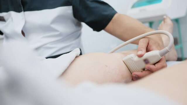 doctor does an ultrasound of the veins on the patient's legs. A phlebologist checks the veins on a woman's legs with an ultrasound machine in a modern clinic.