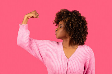 Happy young african american curly woman showing biceps on arm, kissing muscles - obrazy, fototapety, plakaty