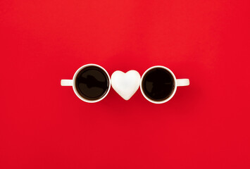 Two white coffee mugs with heart connecting in the form of sunglasses on bright red background....