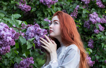 young girl with long red hair in the lilac flowers garden in spring