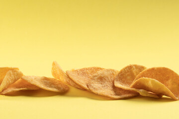 Potato chips scattered on the table close-up on a yellow background. Food with elevated cholesterol levels