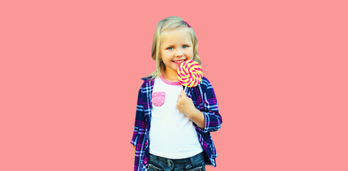 Portrait of happy smiling little girl child with sweet lollipop on stick on pink background