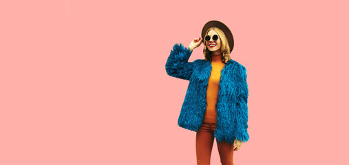 Fashionable portrait of stylish young woman, female model posing wearing blue faux fur, round hat on pink background