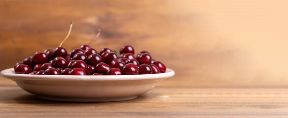 ripe red cherries in a white plate on a wooden background with copy space