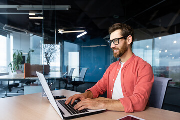 Successful smiling man working inside office with laptop, businessman in red shirt smiling and...