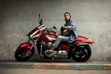 Lifestyle of a motorcyclist, a handsome biker with long hair on a red classic bike in an urban landscape.