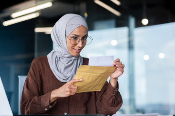 A young happy Arab female student in hijab. Sitting at the desk in the office, holding an envelope with a letter, he received a notification of admission to the university, the results of the exams.