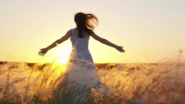 Concept of female dreams, success, travel, flight. Young woman holding her arms to sides runs across field in sun. Happy running girl. Free girl runs happily through meadow in grass in rays of sunset.
