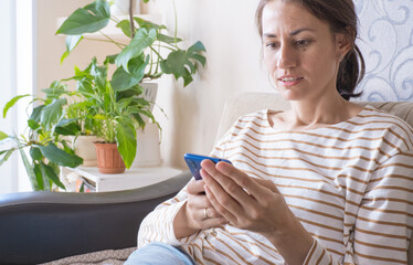 Young woman sit relax on sofa in living room browsing surfing wireless internet on smartphone, millennial girl rest on couch at home message text on modern cellphone, shopping online via website