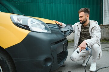 Portrait of a young man standing with charging cable near the charging station