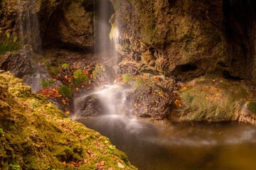 Fototapeta na wymiar forest waterfall in sunlight with autumn leaves