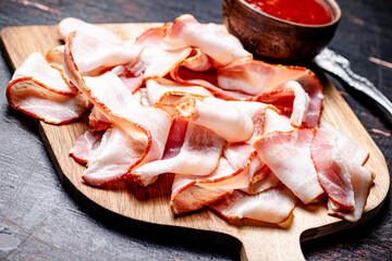 Pieces of bacon on a cutting board with tomato sauce.