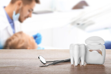 Plastic tooth with dental floss and tools on table in clinic