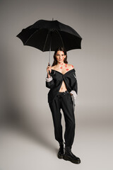 full length of sexy woman with red kiss prints wearing oversize suit while holding umbrella on grey background.