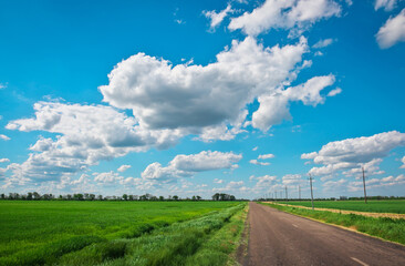 Village Road with power line, green fields and blue sky with clouds