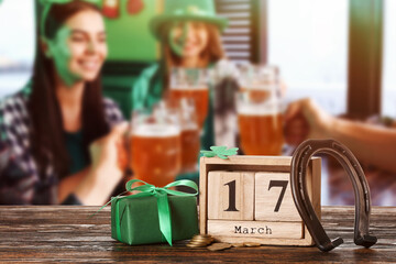Calendar with date of St. Patrick's Day, horseshoe and gift on table in bar