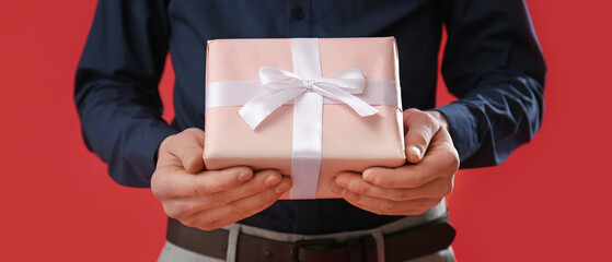 Man holding gift on red background, closeup. Valentine's Day celebration