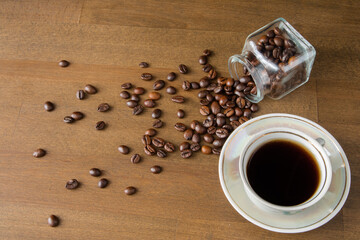 A cup of coffee on a dark wooden table. Spilled coffee beans. Top view.