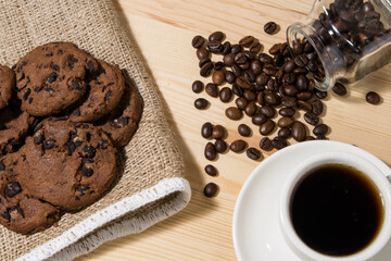 A cup of coffee with chocolate cookie on a wooden table. Spilled coffee beans. Top view.
