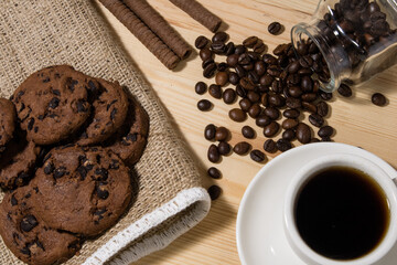 A cup of coffee with chocolate cookie on a wooden table. Spilled coffee beans. Top view.
