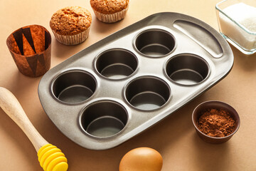 Baking tray with muffins, honey dipper and ingredients on beige background