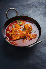 Traditional spicy Indian chicken Madras curry Rogan Josh with drumsticks and wings served as close-up in a korei bowl