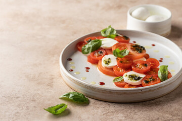 Caprese salad in modern linear feed with tomatoes, basil, mozzarella, pesto, balsamic sauce and olive oil. Traditional Italian food on beige background, copy space