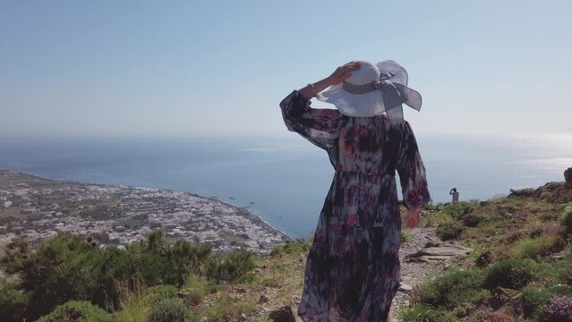 Woman walk on mountain of Ancient Thera in Santorini enjoying aerial panoramic view of Kamari village