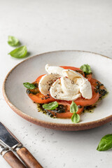 Caprese salad in modern feed with tomatoes, basil, mozzarella, pesto. Traditional Italian food with cutlery on white background with text space, menu