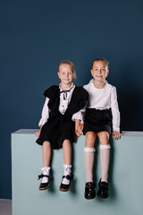 two Smart girls are sitting next to each other in class. Back to school concept. Schoolgirls in black and white school uniform. Trendy background with podium place for text. Primary school education. 